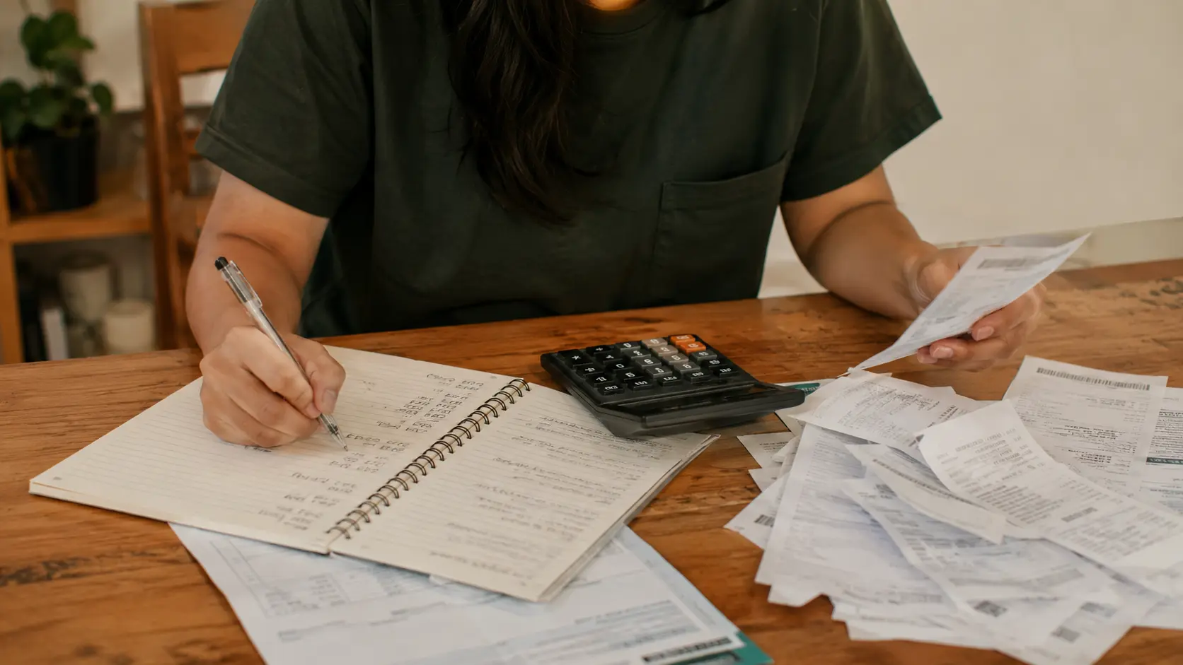 A person at a table with several bills and a notebook, planning the order to pay off multiple debts — representing the debt snowball vs debt avalanche decision